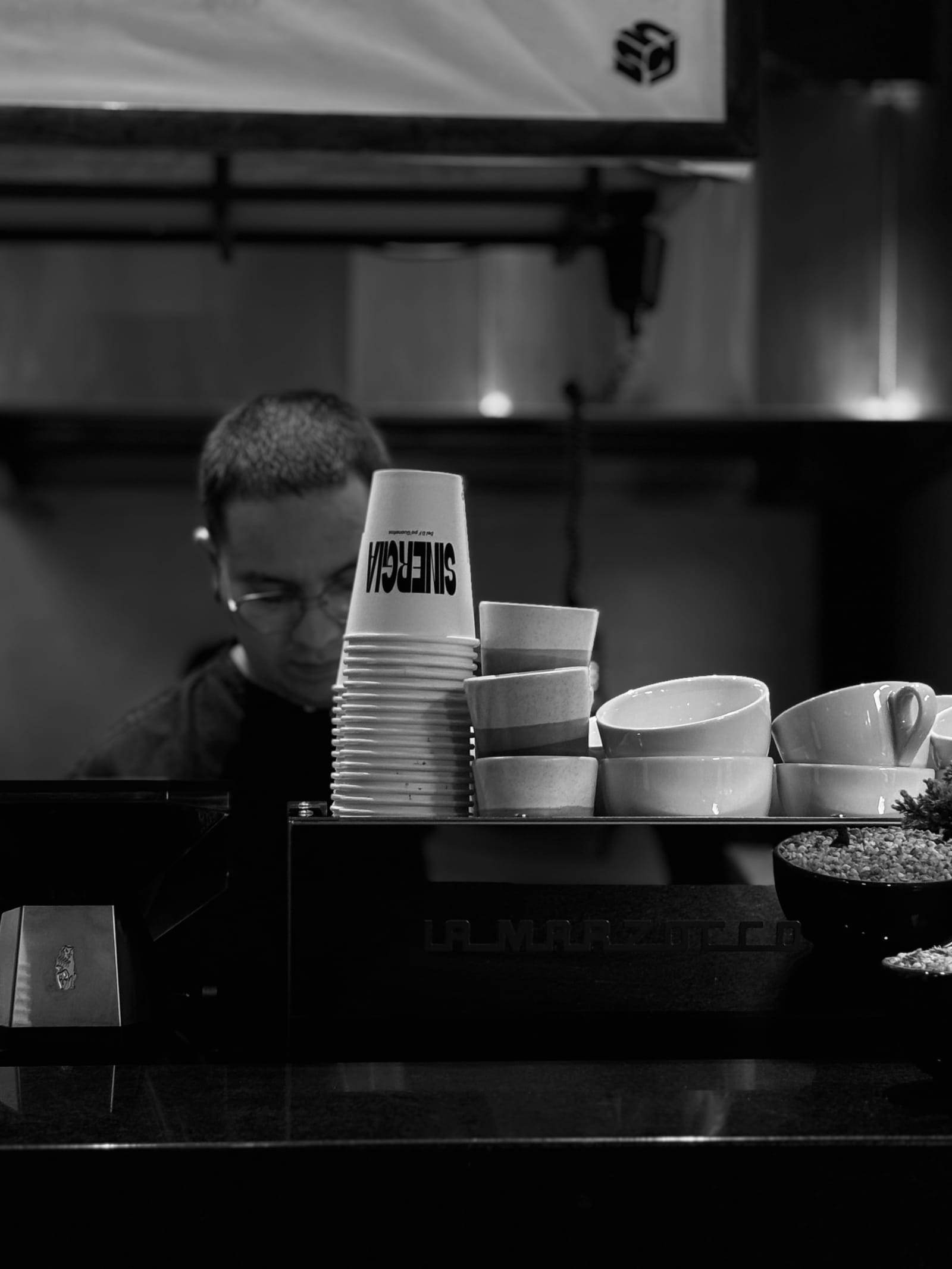 Barista detrás de la barra junto a una torre de vasos y tazas de cerámica