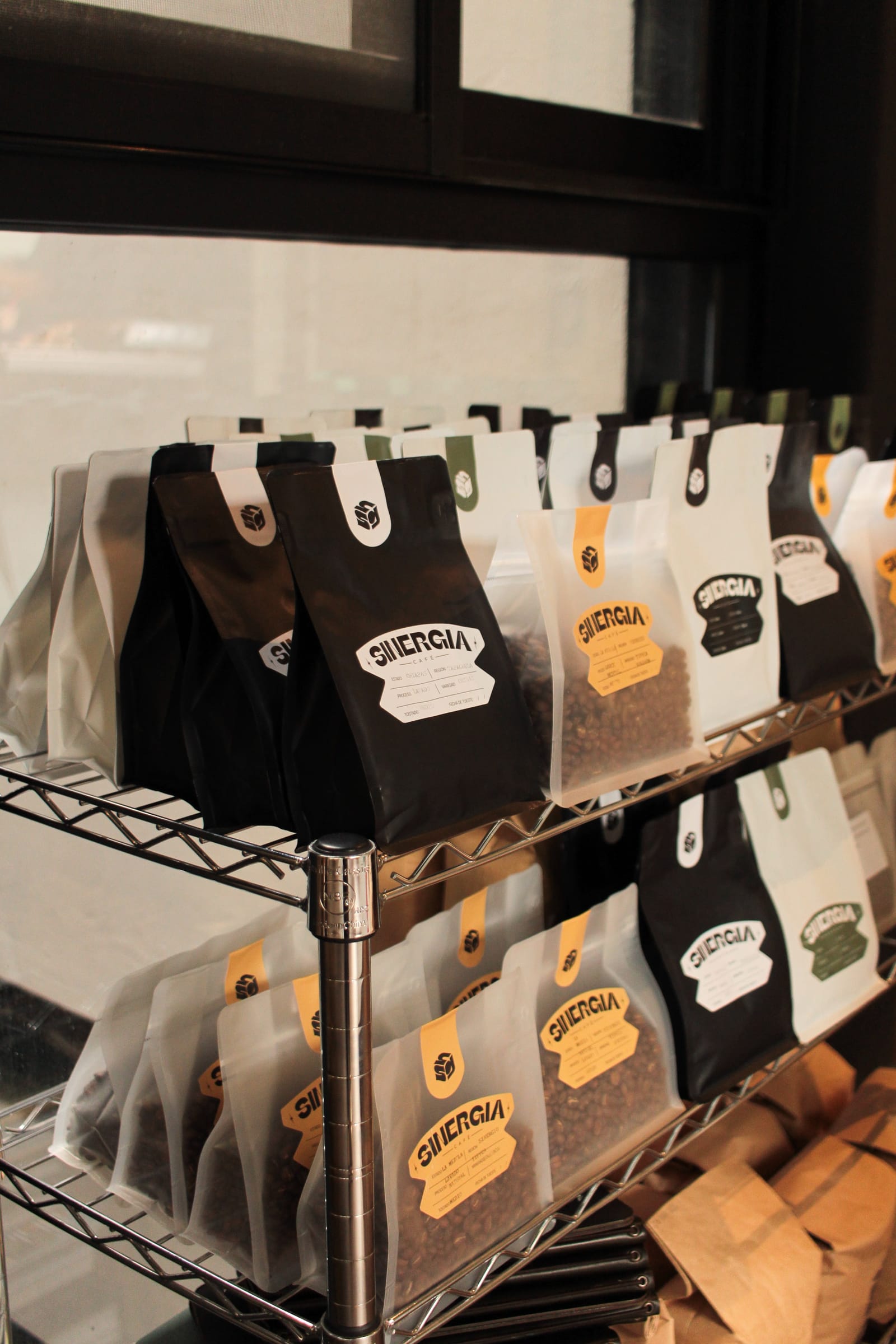 Bolsas de café Sinergia negras y blancas acomodadas en el estante de la tienda