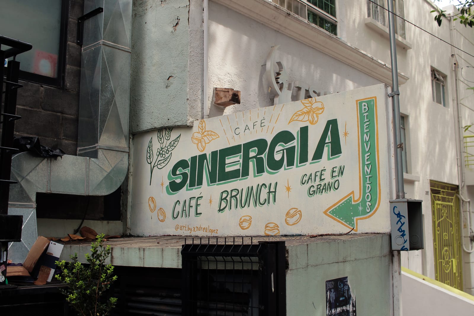 Mural pintado a mano en la fachada de Café Sinergia con la palabra bienvenidos