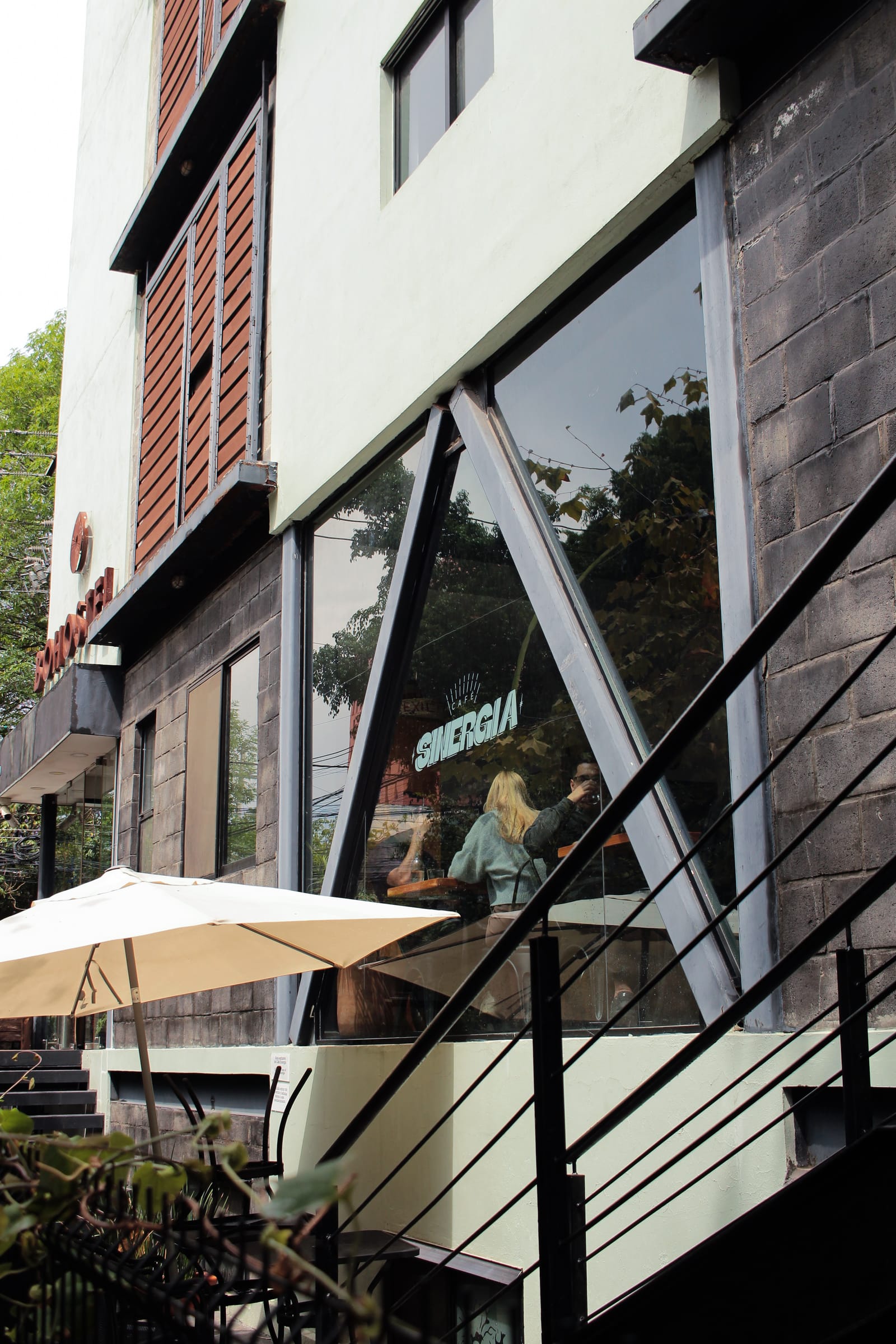 Fachada de Sinergia Café con el logo en el ventanal y la sombrilla de la terraza